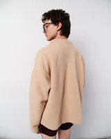 Chaqueta beige simil corderito con cierre frontal, cuello alto y bolsillos de pana marrón con bordados zig zag en hilo rojo y blanco.