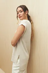 Chaleco color crudo de tejido de punto con cuello redondo y sisas amplias. Tiene corte recto con aberturas laterales en el ruedo.