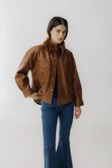 Campera corta de cuero color marrón con cuello de piel sintética color marrón claro, cierre frontal con botones a presión, mangas largas y bolsillos con solapa en el pecho.