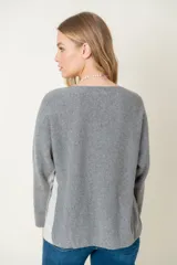 Sweater de lana gris claro con mangas largas y corte holgado. Presenta una franja vertical gris oscuro a lo largo de cada manga.