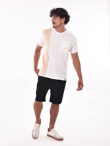 Remera de corte oversize en tonos blanco y beige, con bolsillo en el pecho y estampado en la parte frontal.