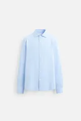 Camisa celeste de corte clásico, confeccionada en tejido de algodón, con cuello italiano abierto, manga larga con puños abotonados y cierre frontal con botones.