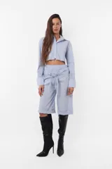 Camisa celeste crop confeccionada en poplín de algodón, con terminación al corte para que desfleque. Acceso a la prenda mediante cartera de botones, cuello y puño reforzado. En canesú de espalda detalle de bordado aplique al corte de logo TW.