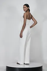 Mono strapless blanco de sastrería con recortes metálicos en el escote, costuras estratégicas y pierna ancha.