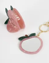 Set de accesorios para el pelo y llavero con espejo, ambos con forma de durazno rosado con hojas verdes.