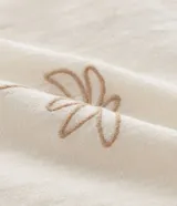 Camisa de hombre con corte boxy, cuello inglés y abotonado delantero. Es de color crema y presenta bordados sutiles de motivos veraniegos en tono naranja claro.