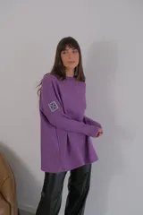 Buzo azul de viscosa con cuello redondo y manga larga. Presenta un aplique con diseño geométrico en el brazo izquierdo.