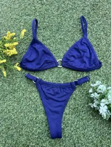 Bikini azul oscuro con tela texturada. El corpiño es triangular con una argolla de zamak en el centro y tirantes finos. La bombacha es colaless con argollas metálicas en los laterales.