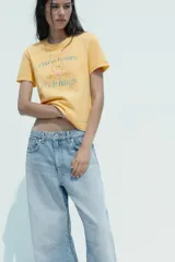 Camiseta color amarillo con efecto lavado, cuello redondo y mangas cortas. Estampado frontal con un oso de los Care Bears™ y la frase "free hugs".