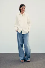 Camisa color crema de corte recto, confeccionada en algodón. Tiene cuello solapa, manga larga con puños abotonados, bolsillo de parche en el pecho y cierre frontal con botones.
