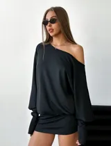 Vestido corto negro elastizado, asimétrico, de manga larga y hombro al descubierto.