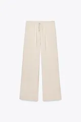 Pantalón de mujer color beige, de corte ancho y tiro medio, confeccionado en tejido fluido. Cuenta con cintura elástica ajustable con cordones, bolsillos laterales y falsos bolsillos de vivo en la espalda.
