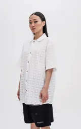 Camisa blanca con textura y botones marrones, de corte holgado y mangas cortas.