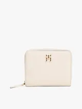 Billetera Tommy Hilfiger color crema con cierre de cremallera y botón a presión. Cuenta con compartimento interior para billetes y múltiples ranuras interiores para tarjetas. Luce el monograma TH metálico en la parte delantera.