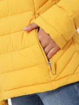 Campera amarilla acolchada con capucha, cierre frontal con cremallera, bolsillos laterales y logo de Tommy Hilfiger en el pecho.