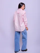 Camisa blanca de algodón, corte holgado, con cuello clásico y botones frontales. Las mangas son largas y se ven remangadas.