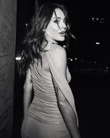 Vestido corto gris de una sola manga con cuello tipo choker. Presenta tejido transparente con hilos plateados brillantes, drapeado en el torso y nudo lateral que genera un efecto cruzado en la falda.