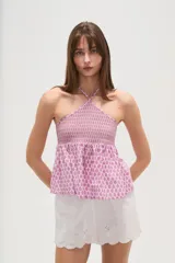 Top sin mangas confeccionado en algodón con estampado integral en tonos rosados. Presenta un diseño con cuello halter cruzado, pechera elástica con técnica de nido de abeja y bajo con volado tipo peplum.