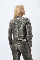 Campera entallada de denim con estampado animal print de cebra en tonos beige y negro. Tiene cuello mao con broches metálicos, cierre frontal con cremallera, bolsillos con cierre en el pecho y mangas largas con puños con cierre.