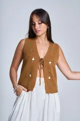 Chaleco tejido color crema con escote en V y cierre frontal con lazos. Presenta bordados de flores en tonos naranja, verde y blanco.