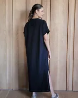 Vestido largo color crudo con cuello redondo y mangas cortas con ribete negro. Tiene corte recto y aberturas laterales en el ruedo.