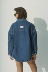 Camisa de denim azul con botones dorados, corte holgado, cuello clásico y bolsillos frontales.