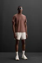 Camiseta deportiva marrón de corte relaxed fit, cuello redondo y manga corta. Presenta paneles laterales de malla negra y logo estampado en la espalda.