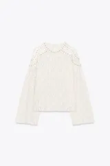 Top de encaje color blanco, con cuello redondo, mangas largas acampanadas y detalle de tachas metálicas en cuello y hombros. Cierre en la espalda con abertura y botón.