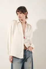 Camisa color blanco hueso de corte fluido, con cuello camisero, mangas largas abullonadas con puño abotonado y detalle de frunces.