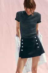 Falda pantalón corta color azul marino, de tiro alto y corte recto. Presenta doble hilera de botones blancos en el frente y cierre lateral con cremallera oculta.