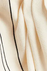 Pollera midi color crema con rayas verticales negras, de punto con textura. Diseño cruzado con elástico oculto en la parte posterior de la pretina y sección delantera cosida con pliegues para crear un leve efecto drapeado.
