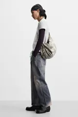 Bolso de hombro color gris con efecto desgastado, fabricado en tejido de algodón. Tiene un compartimento principal con cierre de cremallera, un bolsillo interior con cremallera y asa de hombro ajustable.