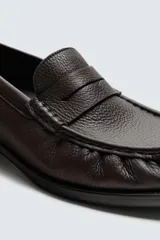 Mocasín de cuero color marrón oscuro con detalle de antifaz en el empeine, plantilla de cuero, horma cuadrada y suela a tono con ligero tacón.