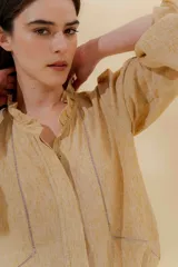 Blusa color beige con cuello mao con volantes, manga larga con puño elástico y cierre frontal con botones ocultos.