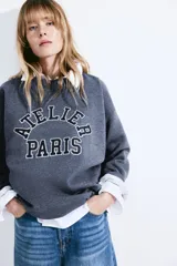 Buzo azul con cuello redondo y mangas largas. Estampado frontal con la frase "Atelier Paris".