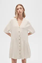 Vestido corto color crema, de corte holgado, con cuello en V y botones frontales.