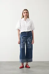 Pantalón de denim azul oscuro con bordado estilo bandana en blanco en los laterales de las piernas y en los puños. El corte es recto y amplio, llegando al tobillo.