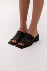 Sandalia marrón de cuero con punta cuadrada, talón abierto y faja ancha. Tiene detalle de elástico oculto en la cara interna de la capellada. El forro y la plantilla son de cuero vacuno.