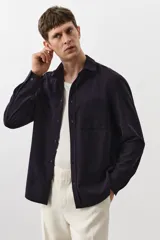Camisa de manga larga color negro con finas rayas verticales, cuello inglés, tapeta clásica, bolsillo superior abierto, canesú con pliegue de caja en la espalda y bajo redondeado.