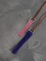 Collar con cordón de cuero marrón y dije cuadrado de metal con flecos rojos.