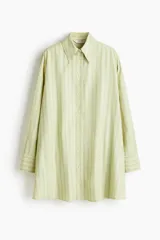 Vestido camisero de manga larga, color verde claro con finas rayas verticales oscuras. Presenta cuello de pico, botonadura frontal y corte evasé/oversized.