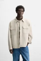 Sobrecamisa color beige de corte relaxed fit, con cuello solapa, manga larga con puños abotonados, bolsillos de plastrón con solapa en el pecho y bolsillos de vivo en la cadera. Cierre frontal con botones.