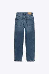 Pantalón de jean azul de tiro alto, corte mom fit, tobillero y con cinco bolsillos. Cierre frontal con cremallera y botón.