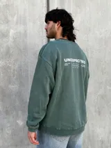 Buzo verde de algodón con cuello redondo, mangas largas y puños acanalados. Presenta un pequeño estampado en el frente y un logo geométrico en el pecho. Corte holgado.