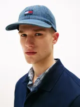 Gorra de béisbol Tommy Jeans confeccionada en denim azul con lavado medio. Presenta el logo de la marca bordado en el frente, ojales de ventilación y costuras texturizadas en la visera.