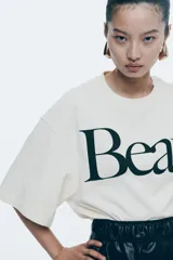 Remera cropped color crudo de corte holgado con cuello redondo acanalado, hombros caídos y bajo recto. Estampado frontal con la palabra 'Beau' en color negro.