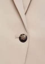 Blazer color beige con cuello de pico con solapa, hombros estructurados, cierre de botón en la parte delantera y dos bolsillos de ribete en la parte delantera.