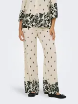 Pantalón de pierna ancha color crema con estampado de hojas negras, cintura elástica trasera y bolsillos frontales.