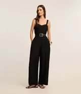 Mono negro de crepé, corte recto y pierna ancha, con escote corazón y tirantes anchos con elástico. Presenta pliegues verticales en el torso y bolsillos laterales.