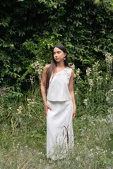 Conjunto blanco de lino, compuesto por un top sin mangas con un solo hombro y detalle de calado, y una falda larga con aberturas frontales y detalle de calado.